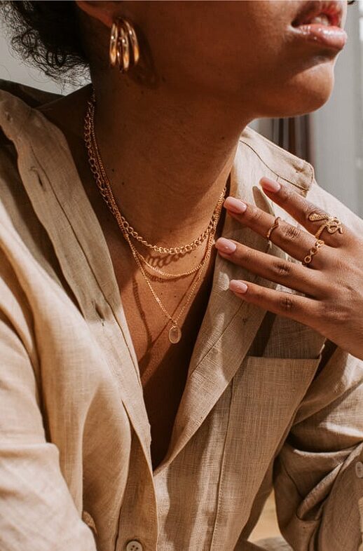 Elegant female portrait featuring a gold jewelry set – delicate chains with a pendant, a ruby ring, and gold earrings from the Dāvana4u collection. Refined style and warm tones highlight the brilliance and quality of the jewelry.